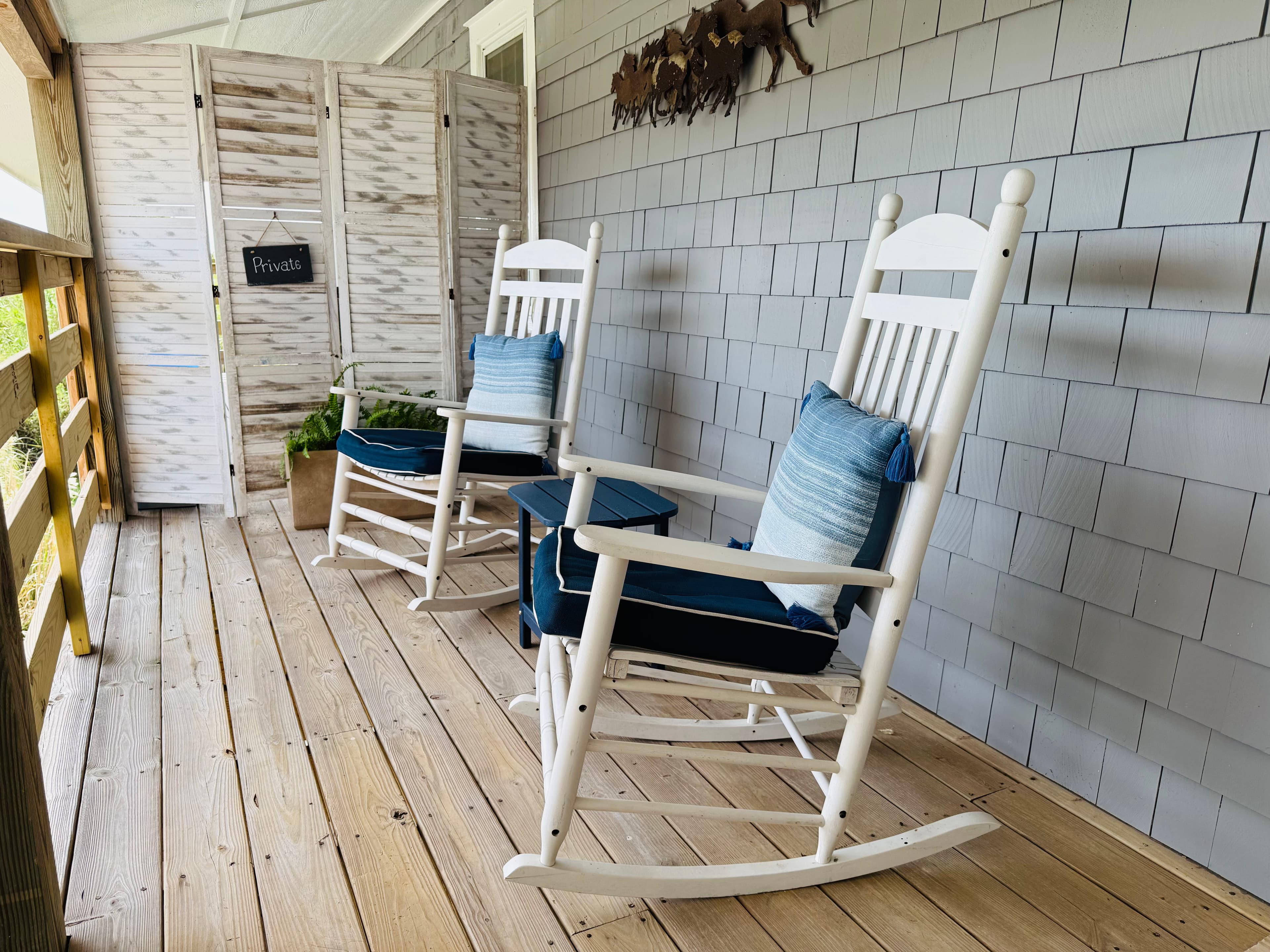 A porch featuring two white rocking chairs with blue cushions and a wooden screen in the background.