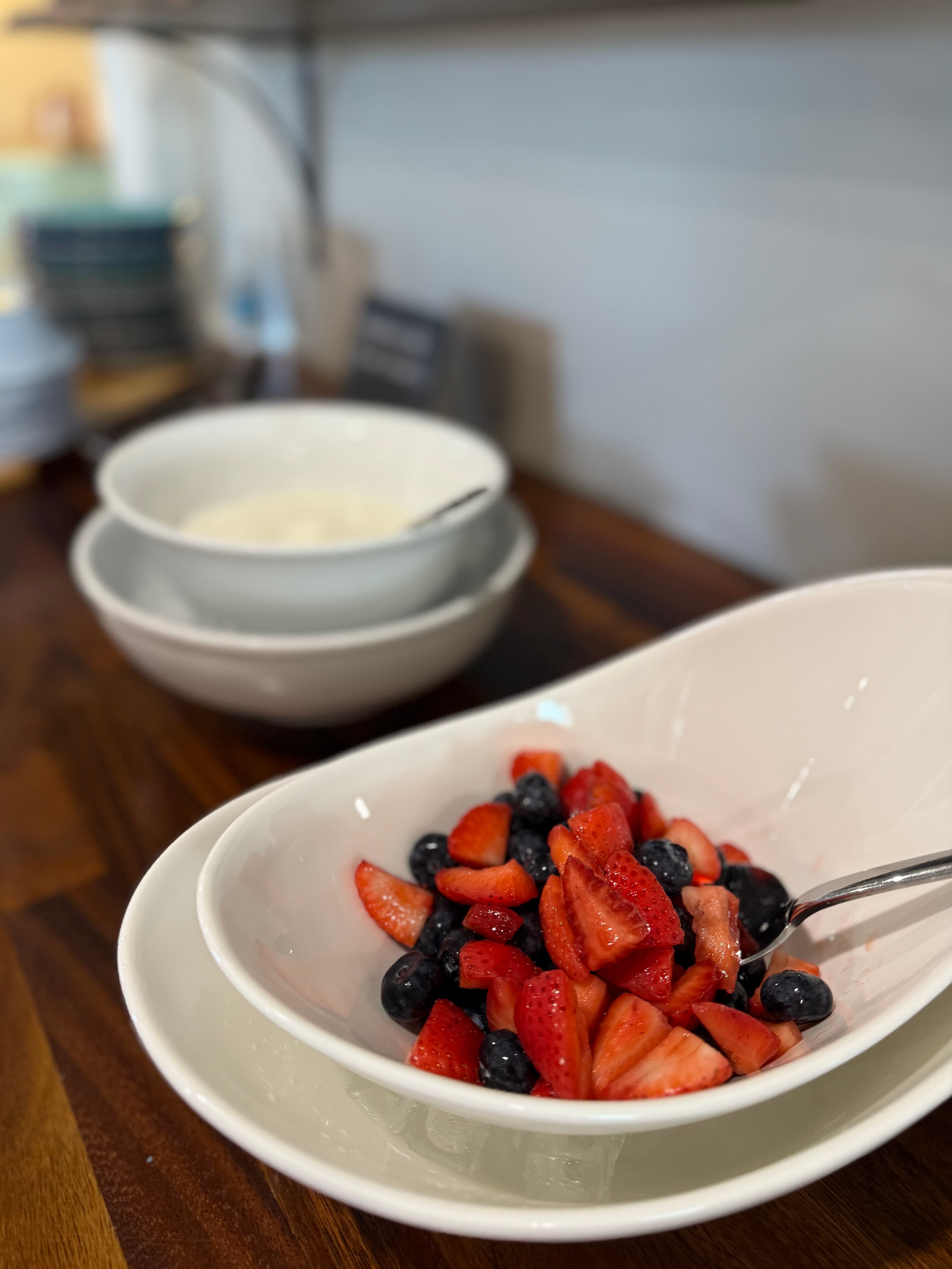 A white bowl filled with sliced strawberries and blueberries, with two empty bowls in the background.