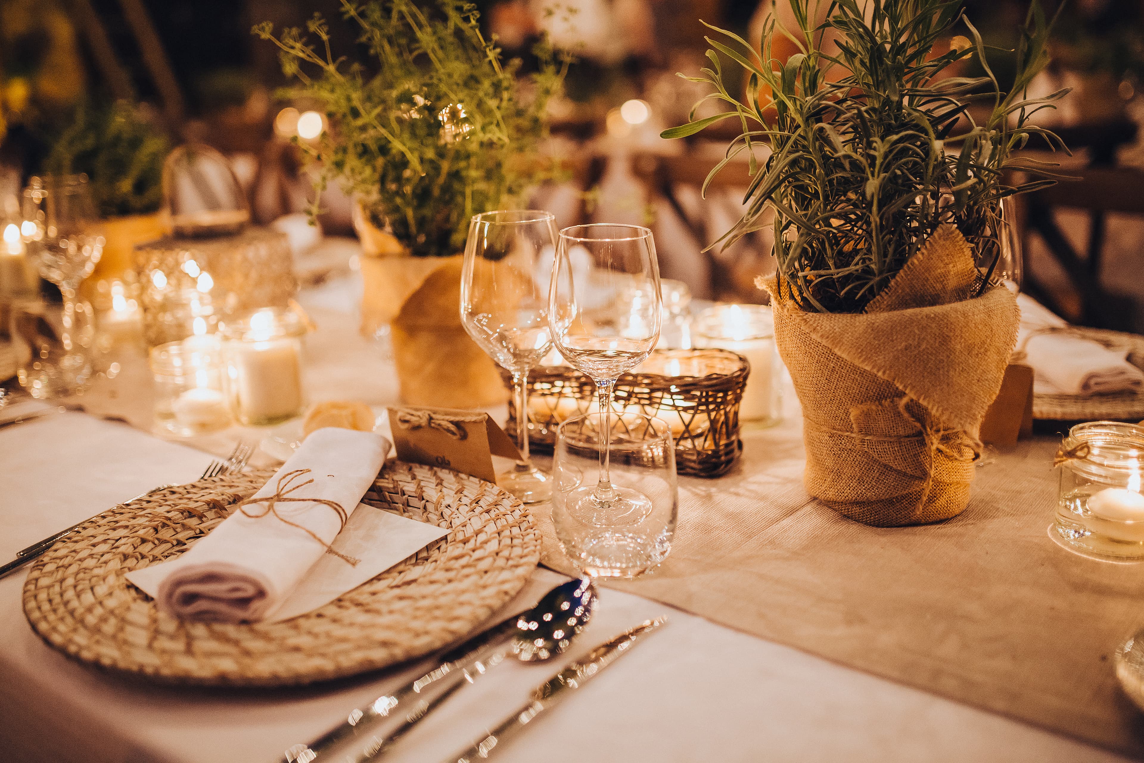 A beautifully arranged table featuring potted herbs, elegant glassware, and softly glowing candles.
