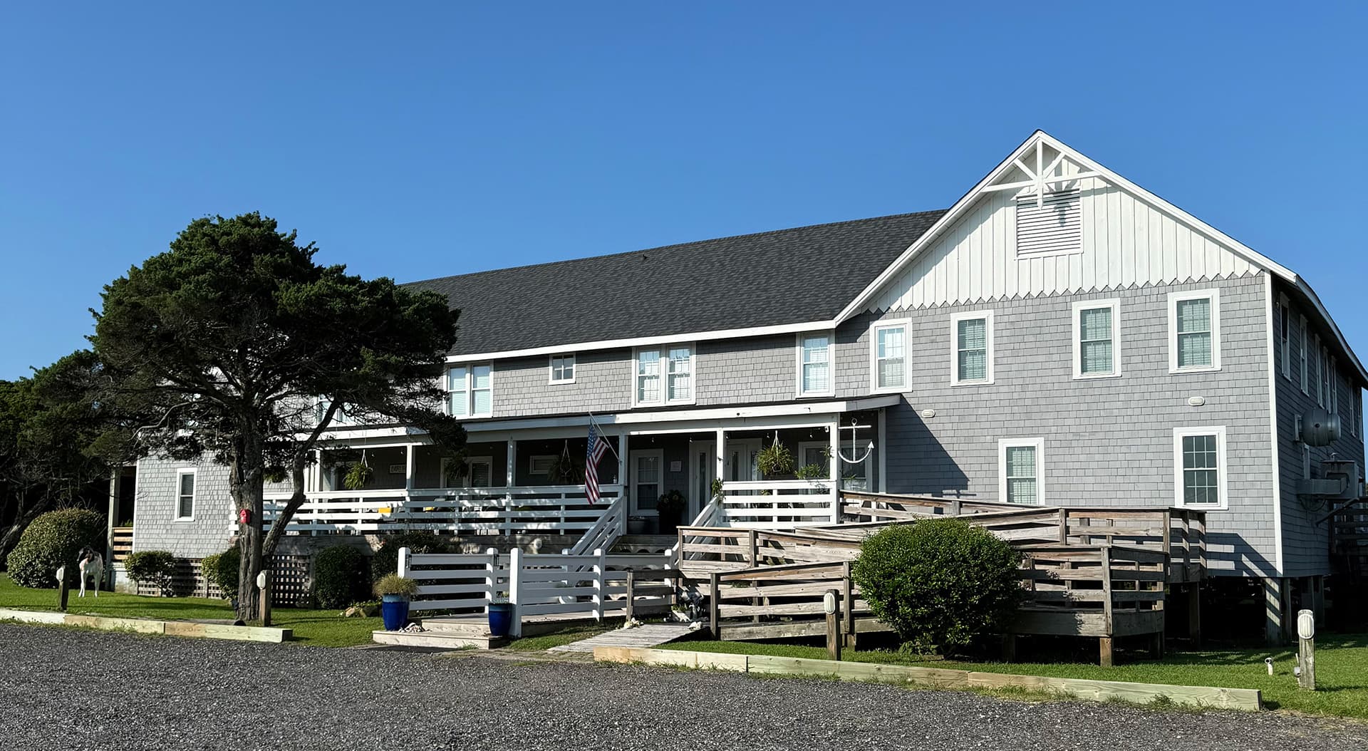 A large, gray-shingled building with multiple balconies and a landscaped entrance under a clear blue sky.