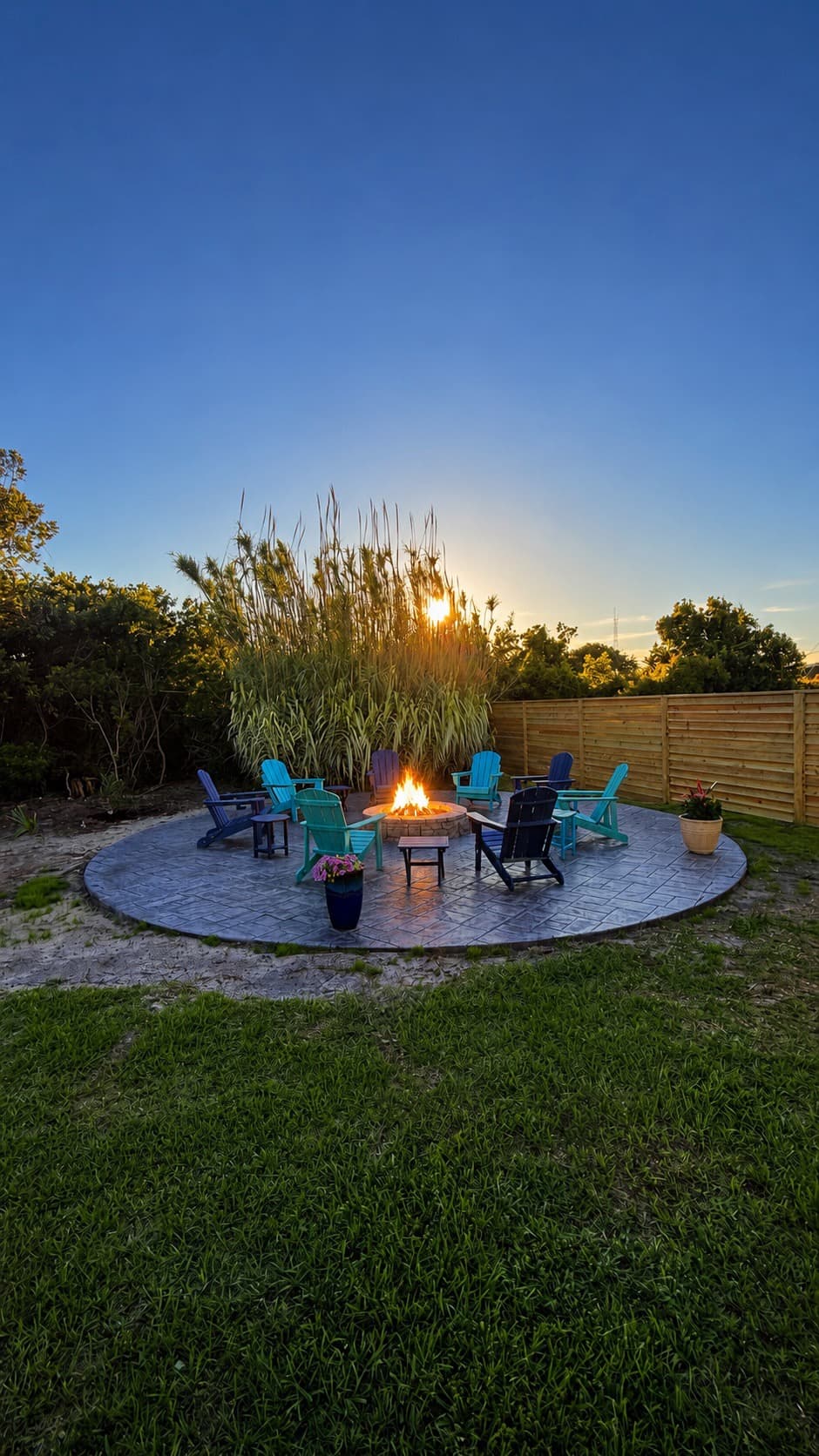 A circular fire pit surrounded by colorful chairs glows under a sunset sky.