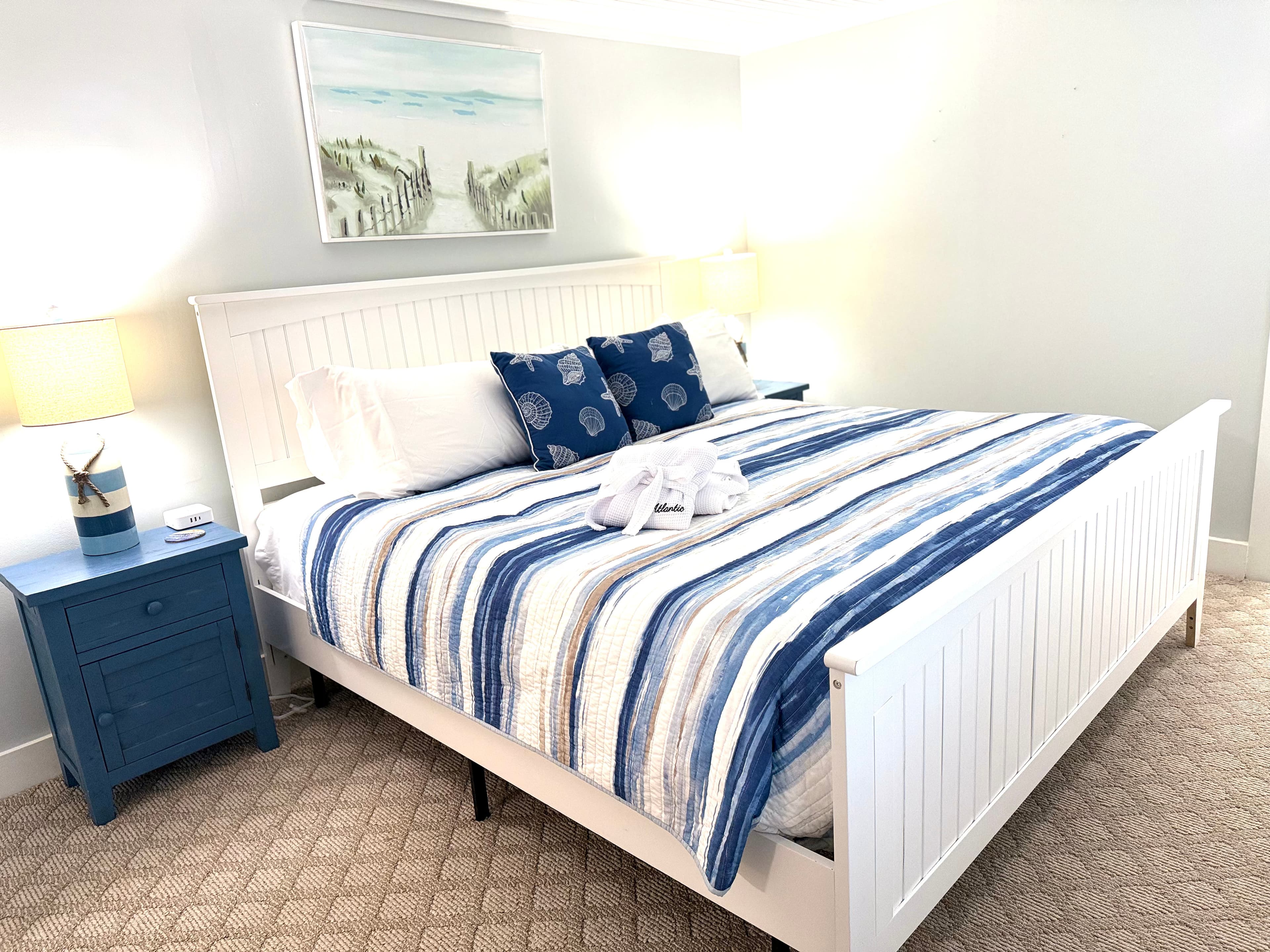 Bright bedroom featuring a striped blue and white quilt, decorative pillows, and a bedside table.
