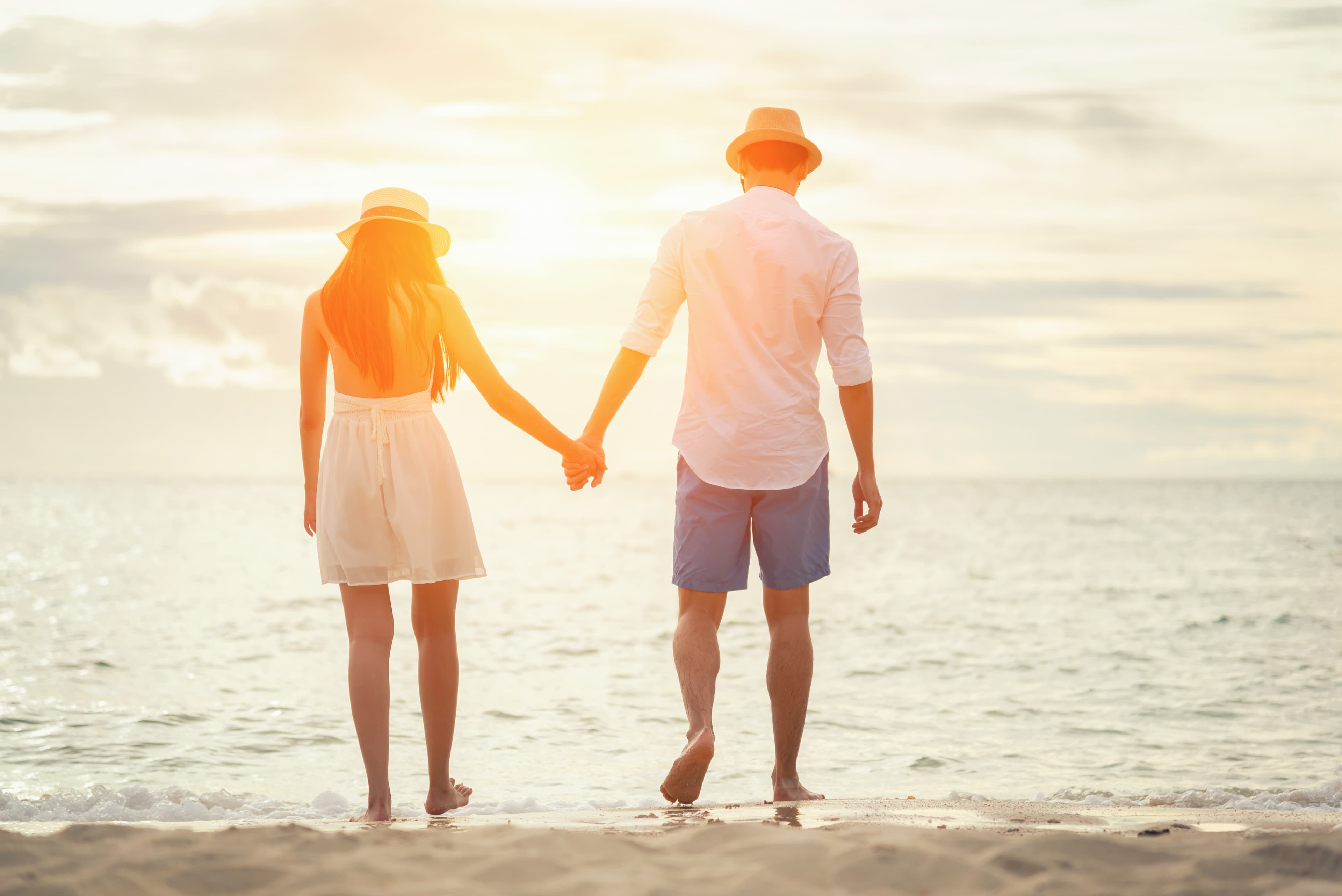 A couple walks hand in hand along a beach at sunset.
