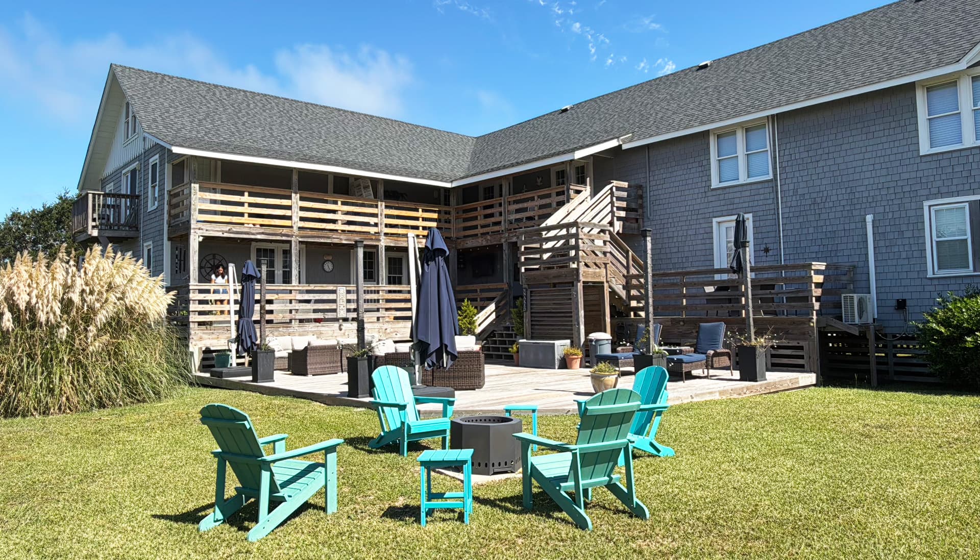 A backyard with turquoise chairs around a fire pit and a multi-level wooden deck.