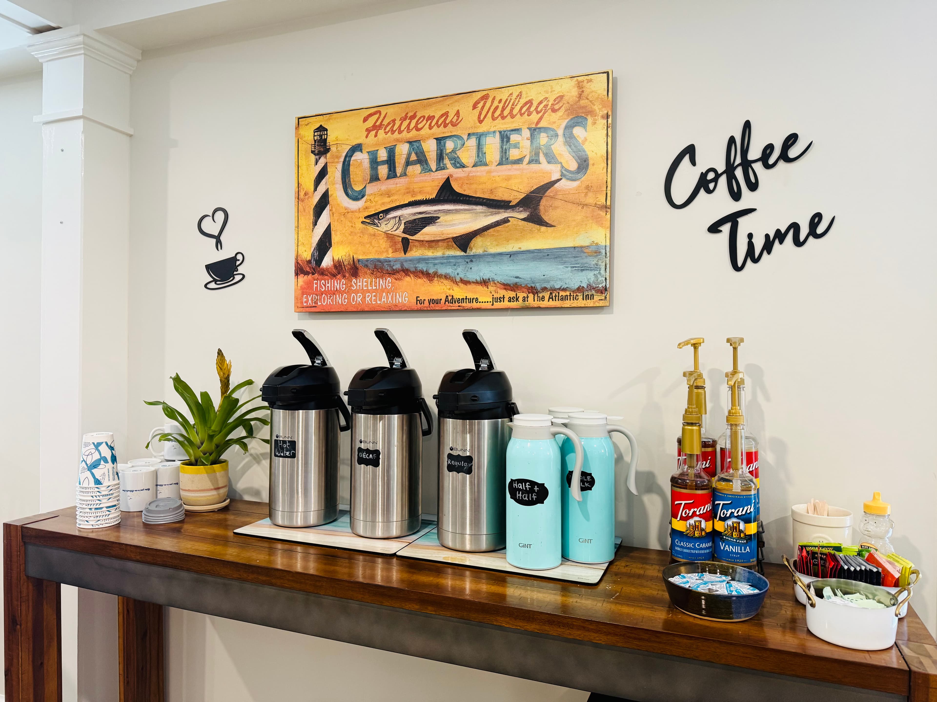 Coffee station featuring multiple dispensers, cups, and a decorative sign.