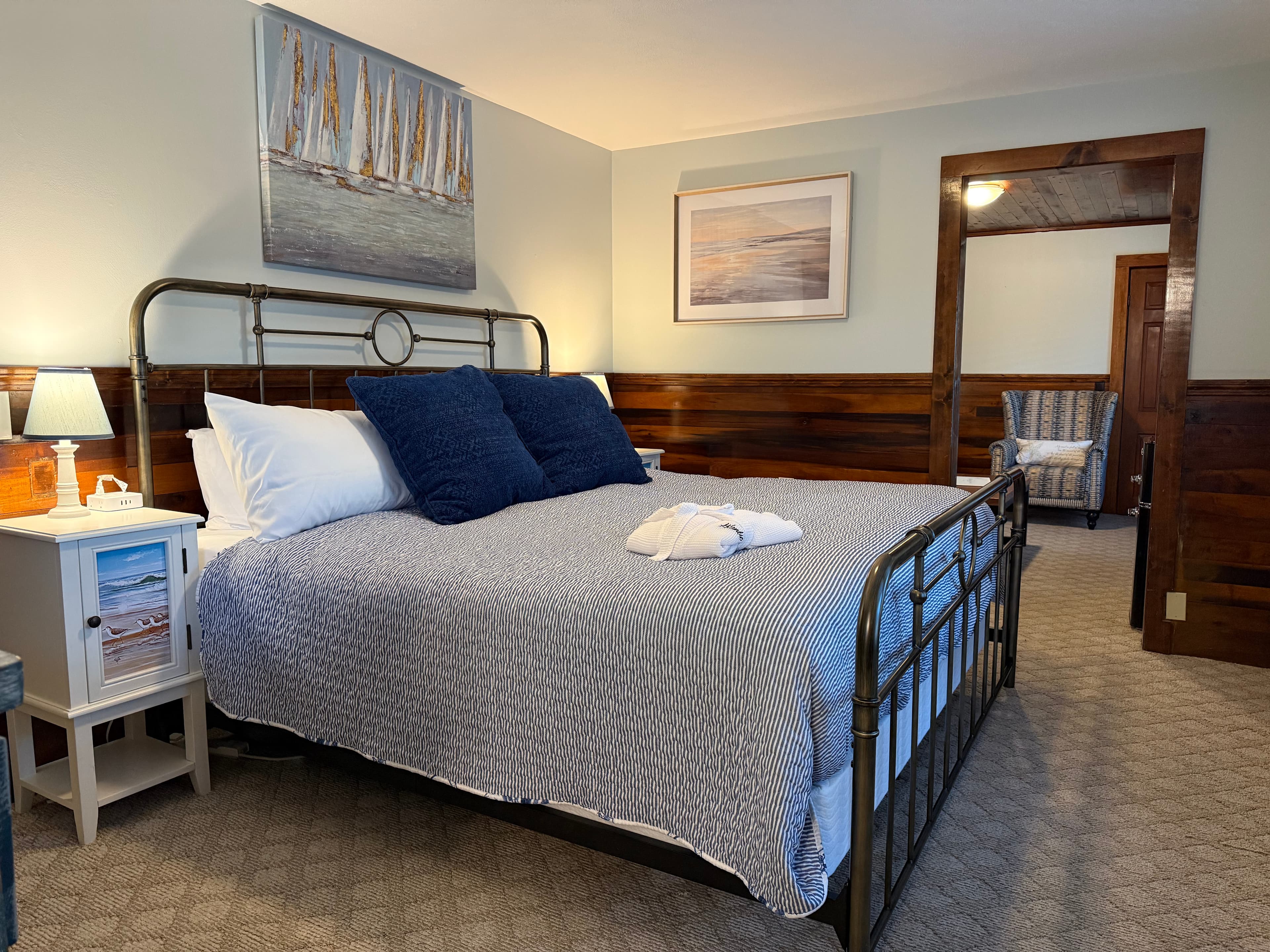 A cozy bedroom featuring a metal bed frame, blue pillows, and nautical-themed artwork.