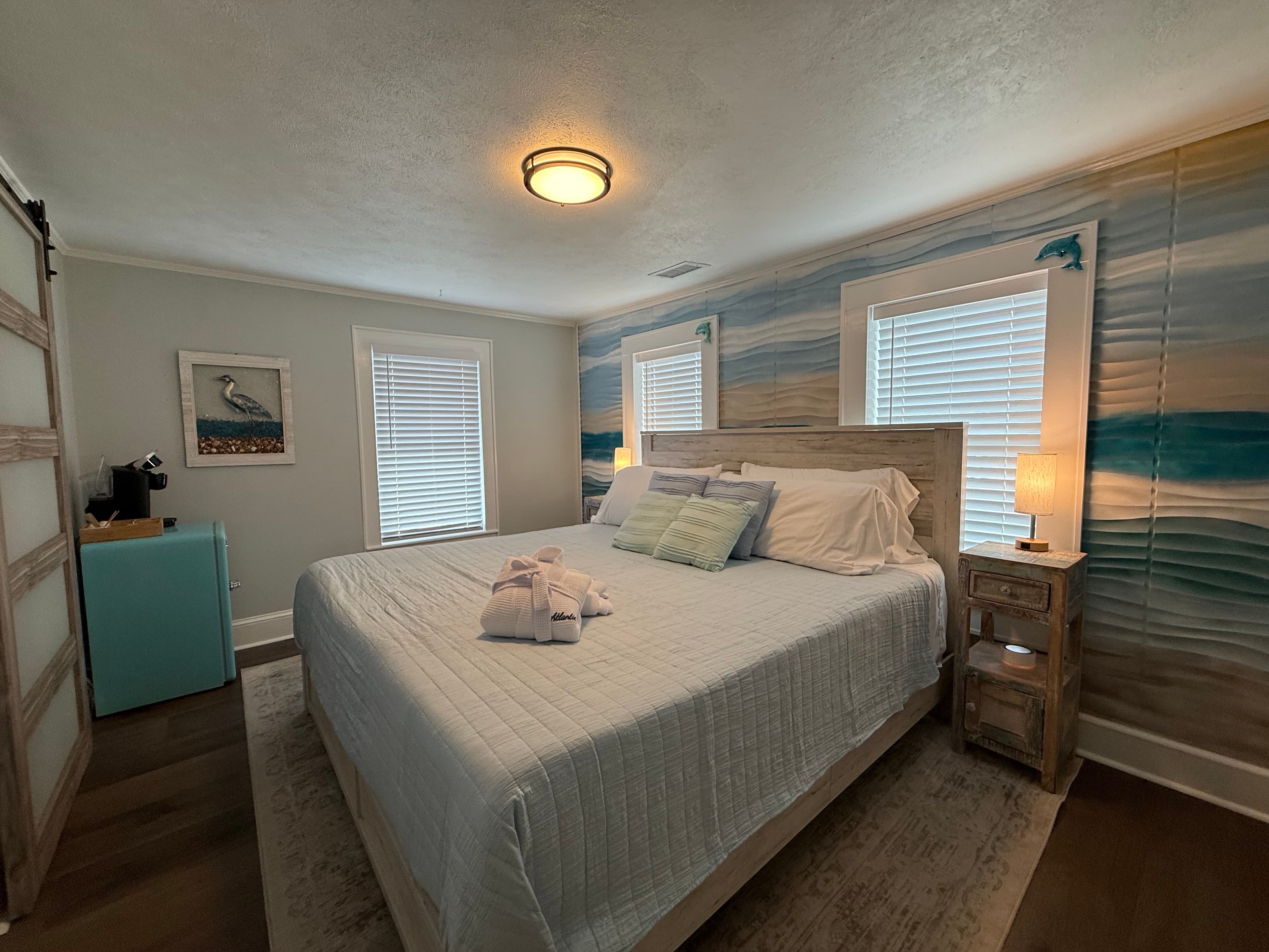 Cozy bedroom featuring a queen bed with light linens, wooden furniture, and coastal-themed decor.
