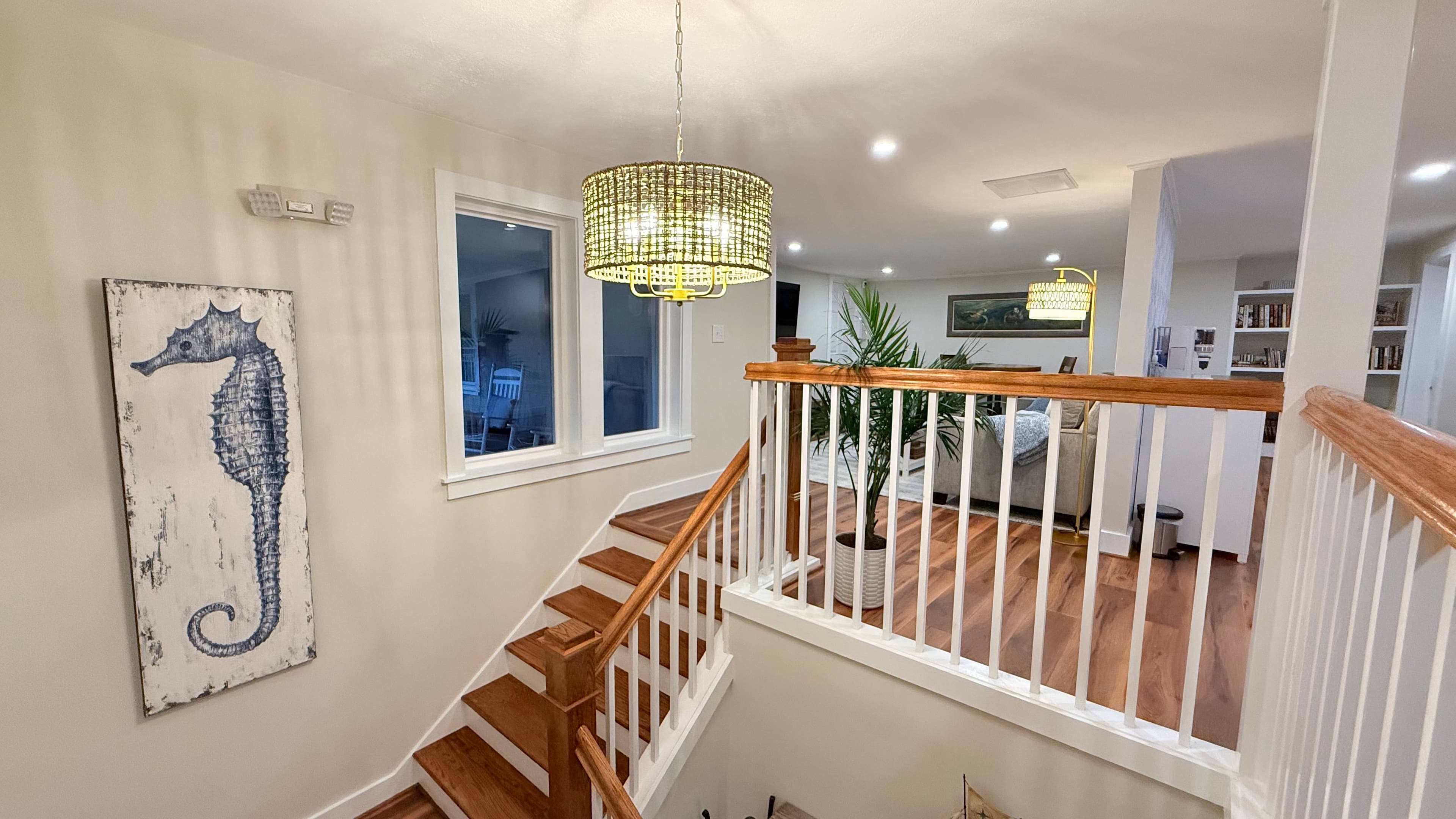 A well-lit staircase leads to a stylish living area, featuring a seahorse painting and modern decor.