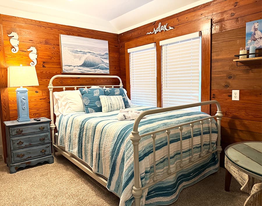 A cozy bedroom featuring a white metal bed with blue and white bedding, a wooden accent wall, and beach-themed decor.