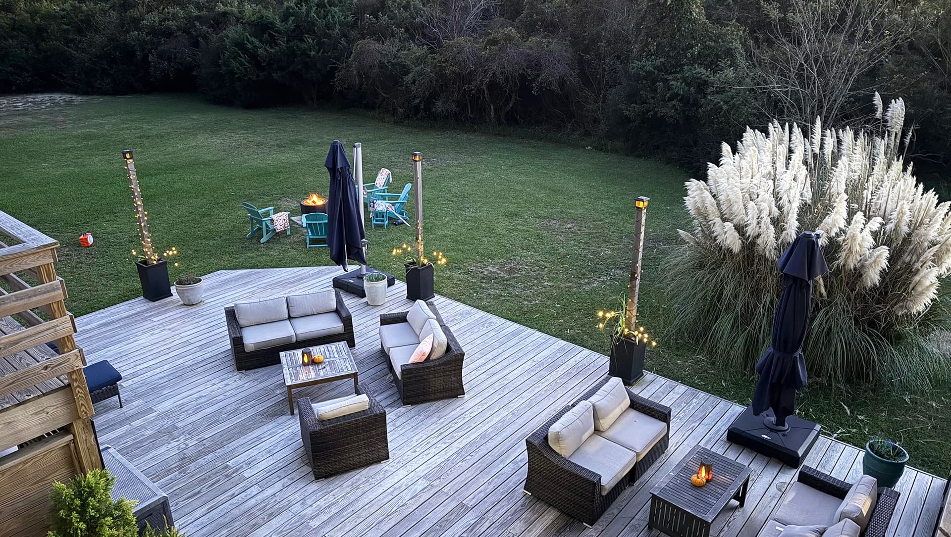 A wooden deck with outdoor furniture overlooks a green lawn and tall grass.